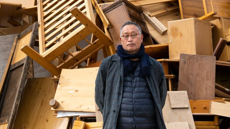 Taiteilija Tadashi Kawamata, seisoo "the Nest" -teoksensa, itseään moninkerroin korkeamman kalusterykelmän, edessä. 