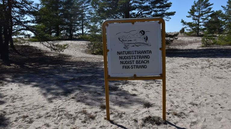 Naturistirannasta kertova kyltti hiekkarannalla.