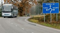 Harmaa linja-auto lähestyy syksyisen sumuisesssa maisema, taustalla bussipysäkki, oikealla liikennemerkki liikenneympyrään, Vehmaa, Turku ja Kalanti.