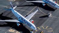 Aerial view of four white Finnair planes parked on a runway in bright weather with green grass in the background.