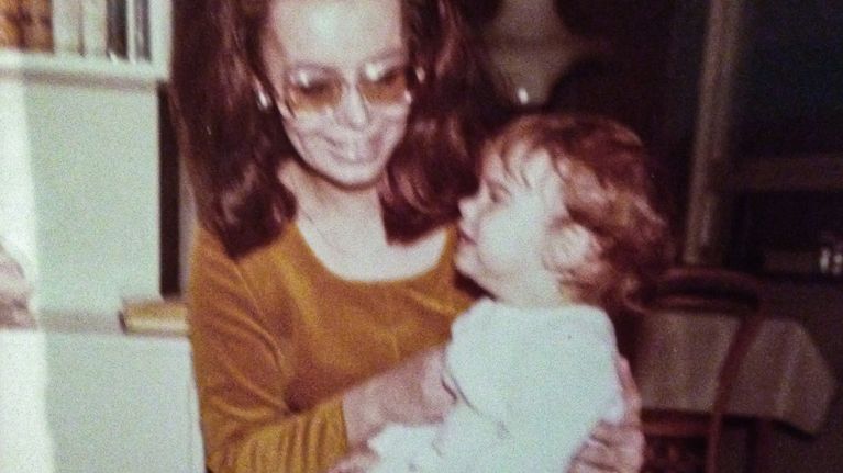 En lite oskarp bild av en liten flicka i sin mammas famn på 1960-talet.