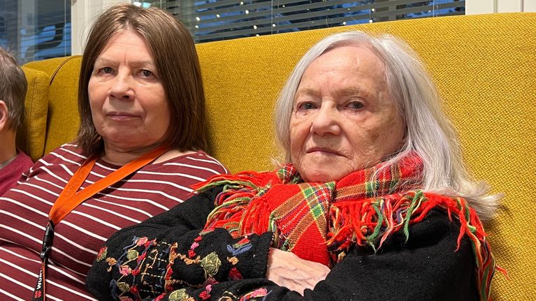 Karen Kitti ja Karin-Marja Rossi istuvat keltaisella sohvalla ja katsovat kameraan Karigasniemen palvelutalolla.