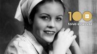 Nuori huivipäinen nainen (näyttelijä Irma Seikkula) hymyilee, kuvassa teksti 100 toive-elokuvaa ja Ylen logo.