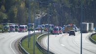 Three fire trucks, two ambulances, a helicopter and other vehicles on a dual-carriage motorway on a sunny day with trees and a rocky cliff behind.