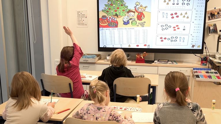 Viisi alakouluikäistä oppilasta opiskelee saamen kieltä koululuokassa ison näytön äärellä.