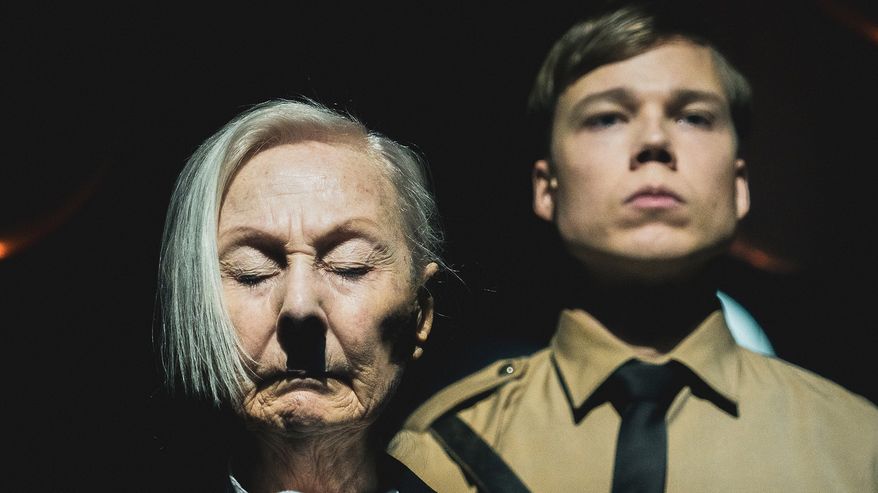 Teatteriesitys, etualalla vanha valkotukkainen nainen, jolla Hilter-viikset, takana nuori mies, joka natsiunivormussa. 
