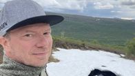 Pentti Pieski katsoo kameraan taustallaan keväinen tunturimaisema.