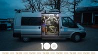 Kuvassa on hämärällä pihalla oleva tuotantoauto, jonka sisällä on kaksi yleläistä työntekijää Yle-takeissa.  Kuvan alalaidassa lukee Yle 100.