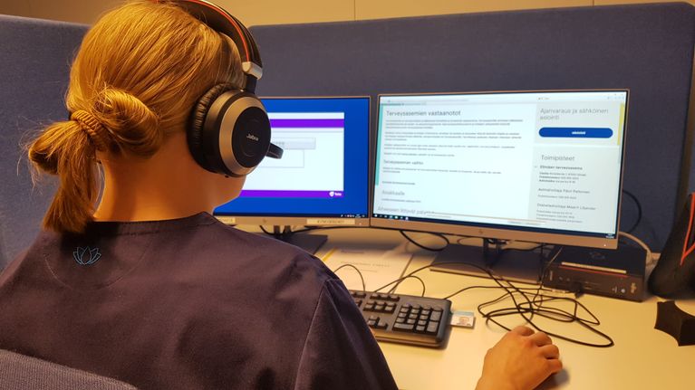 Kymsoten päivystysapupalvelun sairaanhoitaja työpisteellään kuulokemikrofoni päässään.