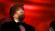 Donald Trump hieman varjossa valon osuessa silmiin punaista taustaa vasten smokissa.