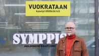 Jarkko Partanen iklädd brun kavaj står framför fönster med texten Symppis. På fönstret finns också en gul lapp med texten "vuokrataan", alltså uthyres.