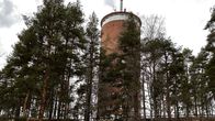 Kuvassa on korkea punatiilinen pyöreä torni keskellä metsää.