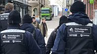 Joukko Nyssen matkalipun tarkastajia kävelemässä Tampereen kadulla. Kaikki ovat selin kameraan ja selissä lukee "Matkalipun tarkastaja".