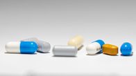 Close-up of 8 pills and tablets of various colours on a white surface. 