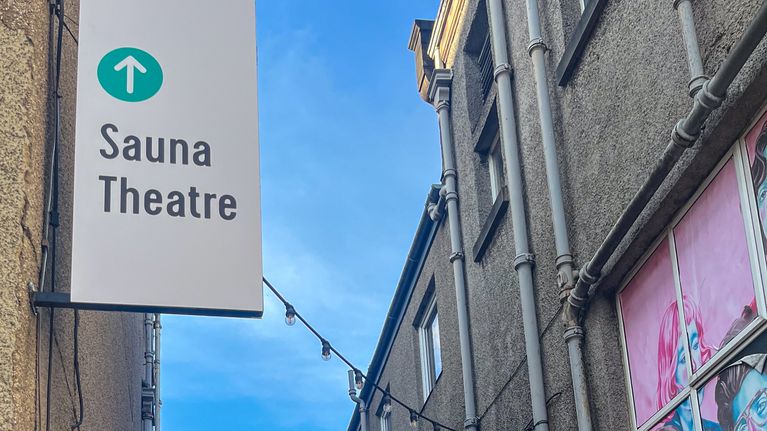 Kapea kujanne, jonka vasemmalla puolella on kyltti ”Sauna Theatre” ja oikealla seinällä värikäs kasvomaalaus.