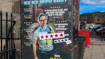 Katukuvassa suuri mainostaulu, jossa mainostetaan MC Hammersmithin esitystä "Ice Ice Nepo Baby"; taulussa tähtiarvioita ja tekstiä.