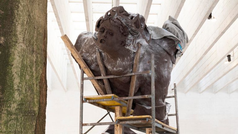 En stor skulptur av en sittande figur omges av byggställningar inomhus.