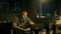 Man sitter vid en dator omringad av flaskor. Ur Harry Hole - Djävulsstjärna.