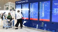 People standing by a large blue airport information display.