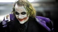 Heath Ledgerin esittämä Jokeri virnistää ja näyttää pelikorttia, jossa on jokerin kuva.