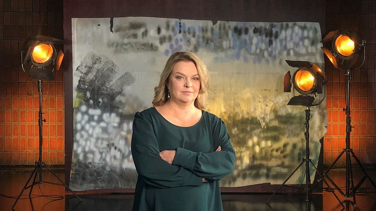 Elina Knihtilä seisoo studiossa taustalavasteen ja studiolamppujen edessä. Kuva otettu lyhytvideosarjaan Me elokuvantekijät.