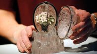 Ett Fabergéägg i kristall och diamanter med en bukett vitsippor inuti hålls öppet av två händer.