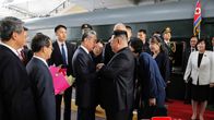 Kim Jong-un takanaan Kim Ju-ae tummissa puvuissa punaisella matolla virallisen vastaanottokomitean tervehdittävänä.