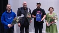 Neljä kukilla ja kunniakirjalla palkittua miestä ja nainen seisomassa juhlasalissa.