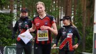 Kolme suunnistajaa lähestyy maalialuetta metsän keskellä; taustalla viestiliiga-maali ja sponsoreiden logot.