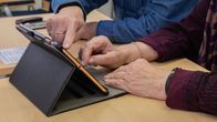 Seniorit tutkivat tablettia pöydän ääressä.