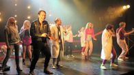 Joukko nuoria tanssii värivaloissa teatterin näyttämöllä