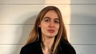 En person med långt blont hår och en svart topp sitter mot en vägg och badar i varmt ljus.