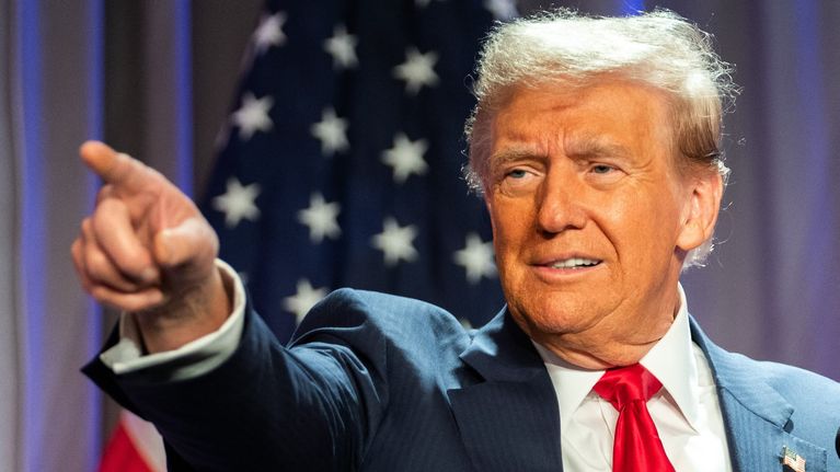 Donald Trump osoittaa oikean käden sormellaan, taustalla tähtilippu.