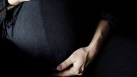Detail photo of a pregnant woman's abdomen. She is wearing a black top and her hands can be seen cradling her belly.