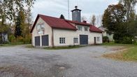 Vaalea kivirakennus, jossa punainen katto ja useita suljettuja ovia, seisoo tyhjällä sorapihalla.
