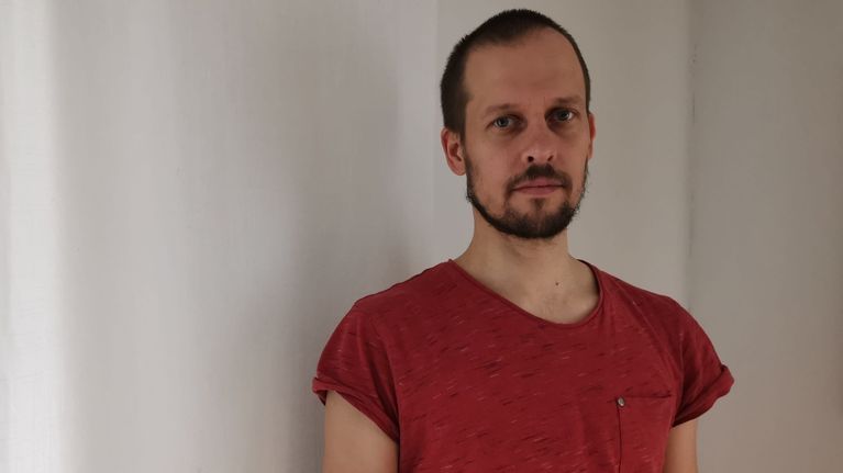 Mies poseeraa vaalean seinän edessä