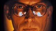Silmälasipäinen mies (Peter Weller) katsoo suoraan kohti erikoislähikuvassa. Kuva elokuvasta Alaston lounas