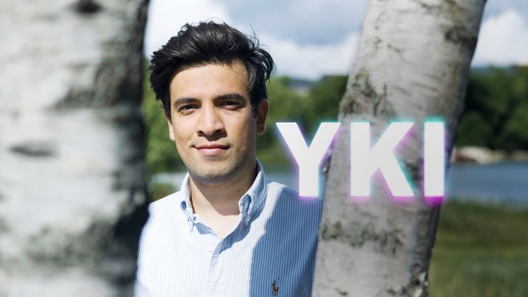 Mies poseeraa kahden koivun välillä, kuvan päällä on YKI-teksti.
