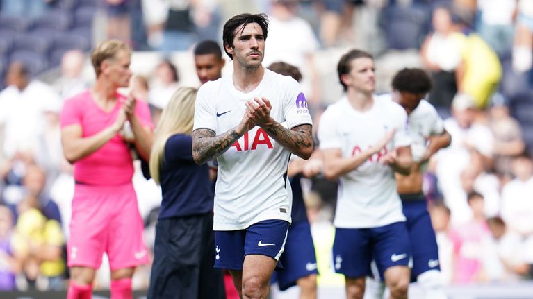 Flera fotbollsspelare i Tottenham Hotspur-tröjor står på en fotbollsplan och applåderar.