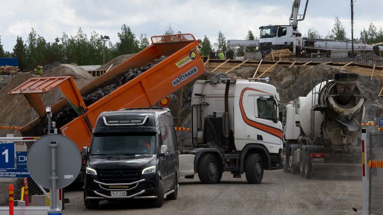Työmaa-alueella suoritetaan sillanrakennustöitä, joissa käytetään betoniautoja ja nostokalustoa.