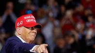 Vanha mies osoittaa oikealla kädellään lähikuavssa oikealle. Hänellä on laimea virnistys kasvoillaan ja päässään punavalkoinen lippalakki, jossa lukee: 45-47 MAKE AMERICA GREAT AGAIN.