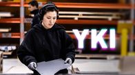 Nainen tekee metallitöitä kuulosuojaimet päässään, kuvan päällä on YKI-teksti.