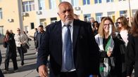 Boiko Borisov kävelee aurinkoisena päivänä ulkona puku päällään perässä kävelee ihmisiä, joista osa kuvaa tilannetta.