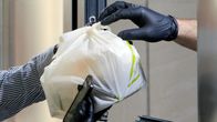 Ett matbud hämtar ett maketpaket från en restaurang i Bukarest mitt under coronaepidemin. Både matbudet och restaurangpersonalen bär skyddshandskar.