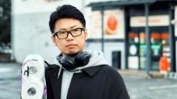 Japanissa syntynyt koomikko Gen Takagi seisoo ruokakaupan edessä vessapaperipaketti kainalossaan.
