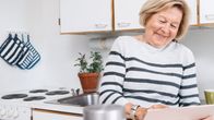 Hymyilevä nainen tutkii tablettitietokoneen ruutua keittiössä. Kuvituskuva.