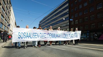 Ihmiset marssivat kadulla ja pitelevät banneria, jossa lukee "sosiaalisen oikeudenmukaisuuden puolesta!"