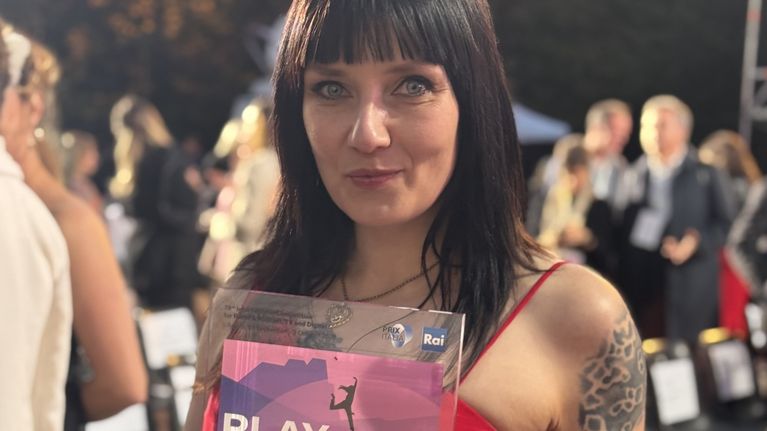 Kuvassa on nainen, joka pit�� k�siss��n lasista palkintoa.