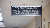 Kuvassa katosta roikkuva kyltti Kokkolan poliisiasemalla. Kyltissä lukee ota palvelunumero