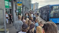 Ihmiset jonottavat kauppakeskuksen sisäänkäynnin edessä, taustalla linja-auto 553.
